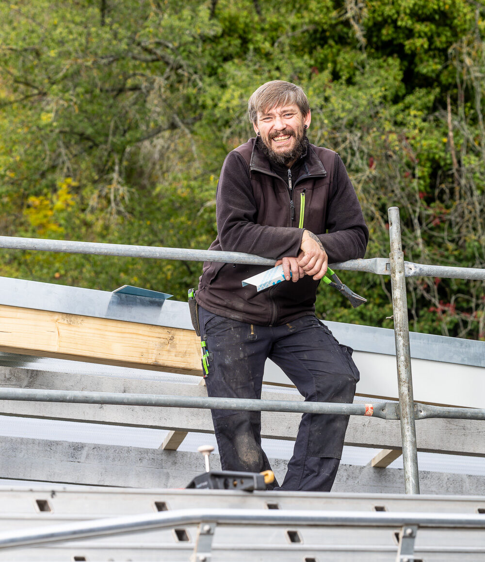 Handwerker steht auf einem Dach, Dachdecker, lächelt in die Kamera